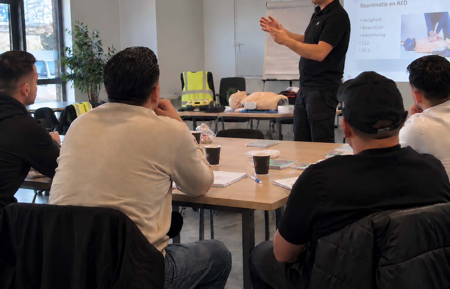 Kleine groep tijdens een interactieve BHV/EHBO-training, geobserveerd van achteren